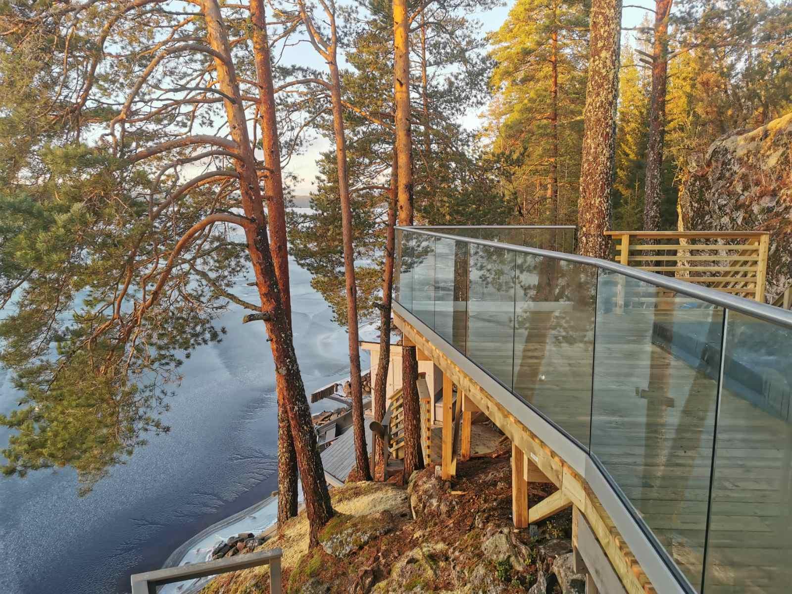 En moderne gangvei av glass som strekker seg langs en innsjø, omkranset av høye trær og naturskjønn utsikt.