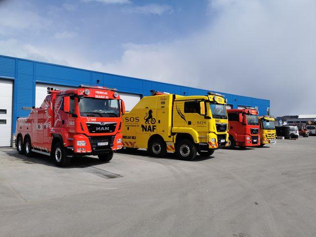 Flere lastebiler i forskjellige farger parkert foran en lagerbygning.