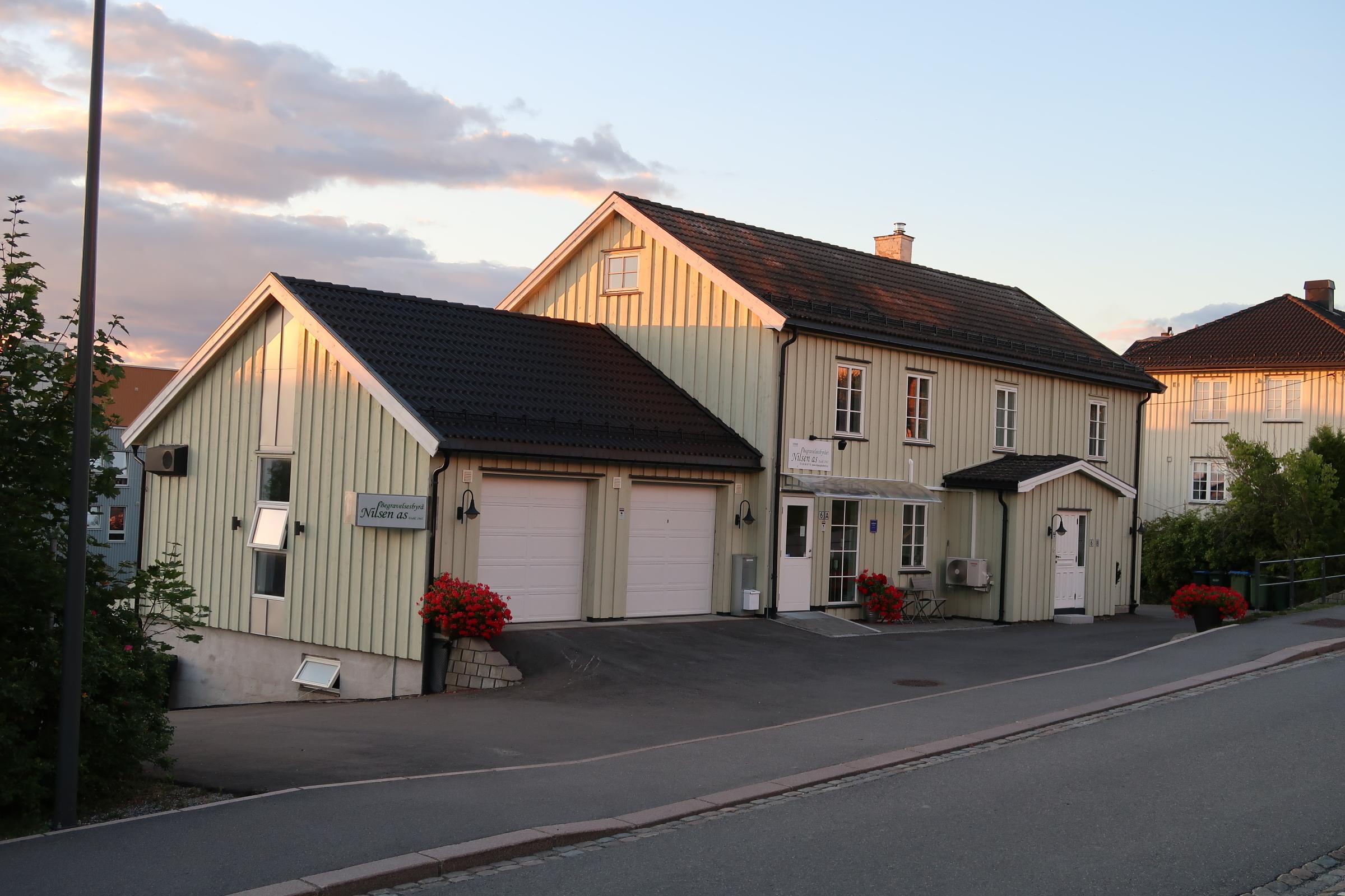 En sjarmerende, gulstripet bygning med garasje og hage, beliggende ved en vei i solnedgang.