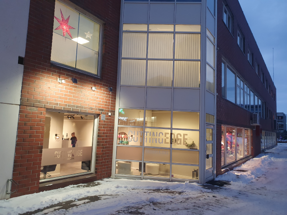 En moderne bygning med store vinduer, snø på bakken og juledekorasjoner i vinduene.