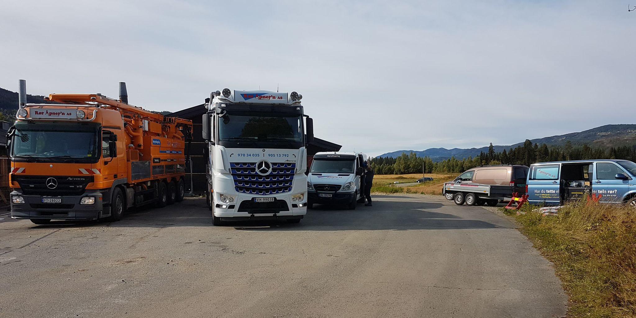 Tre lastebiler står parkert på en vei med fjell i bakgrunnen, en av dem er en hvit Mercedes.