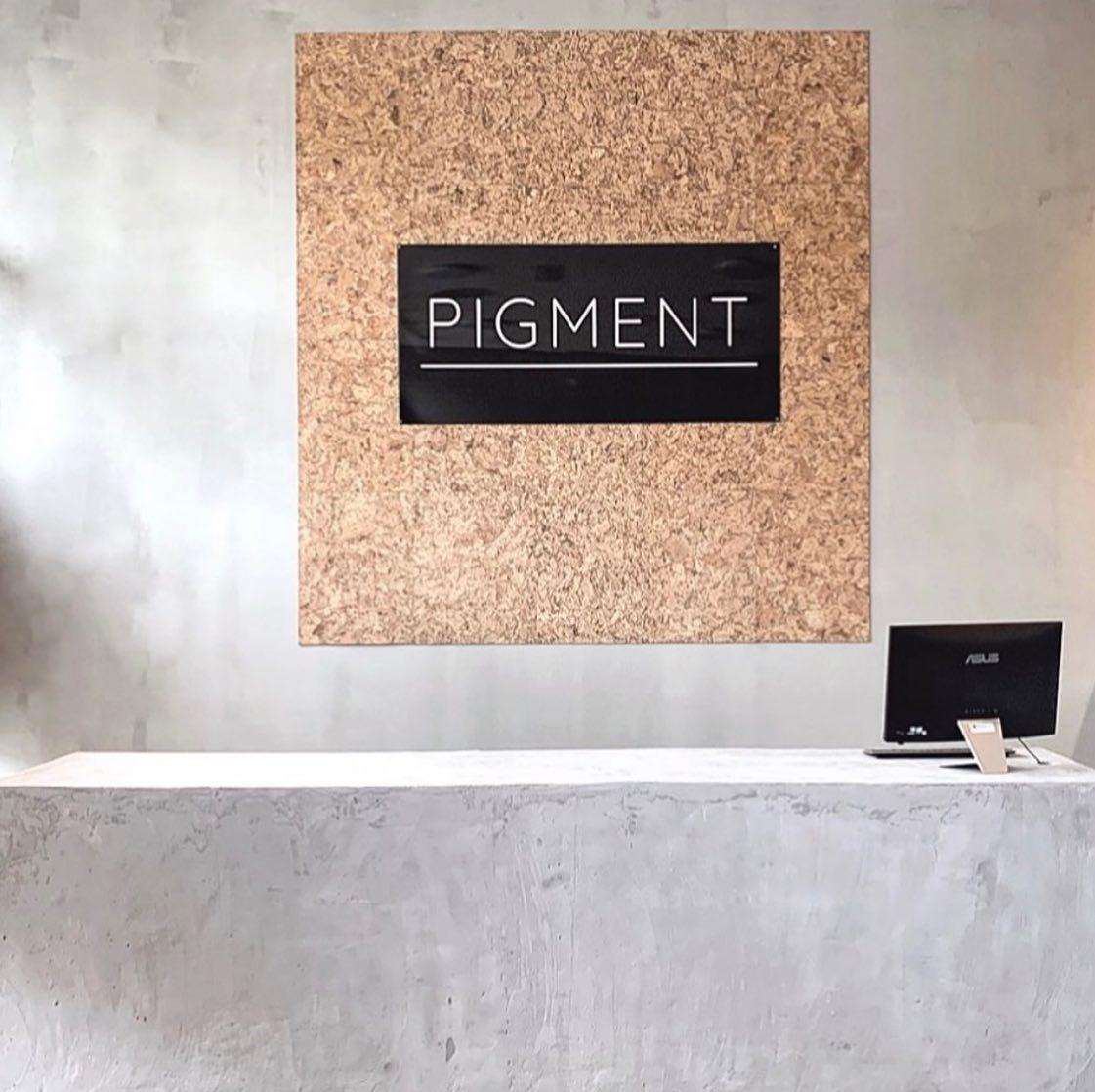 Moderne resepsjon med en stor korktavle og skiltet "PIGMENT" over en betongdisk.