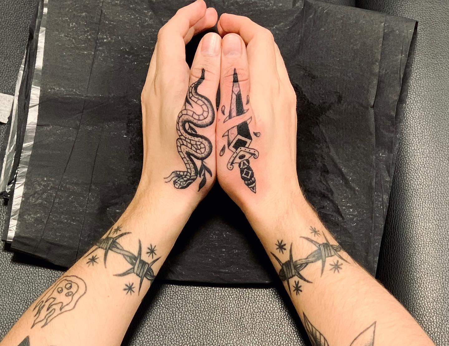 Hender med tatoveringer av en slange og en blyant, samt flere tatoveringer på underarmene.