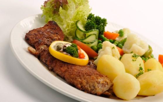 En tallerken med stekt fisk, poteter, grønnsaker og salat, dekorert med sitron og persille.