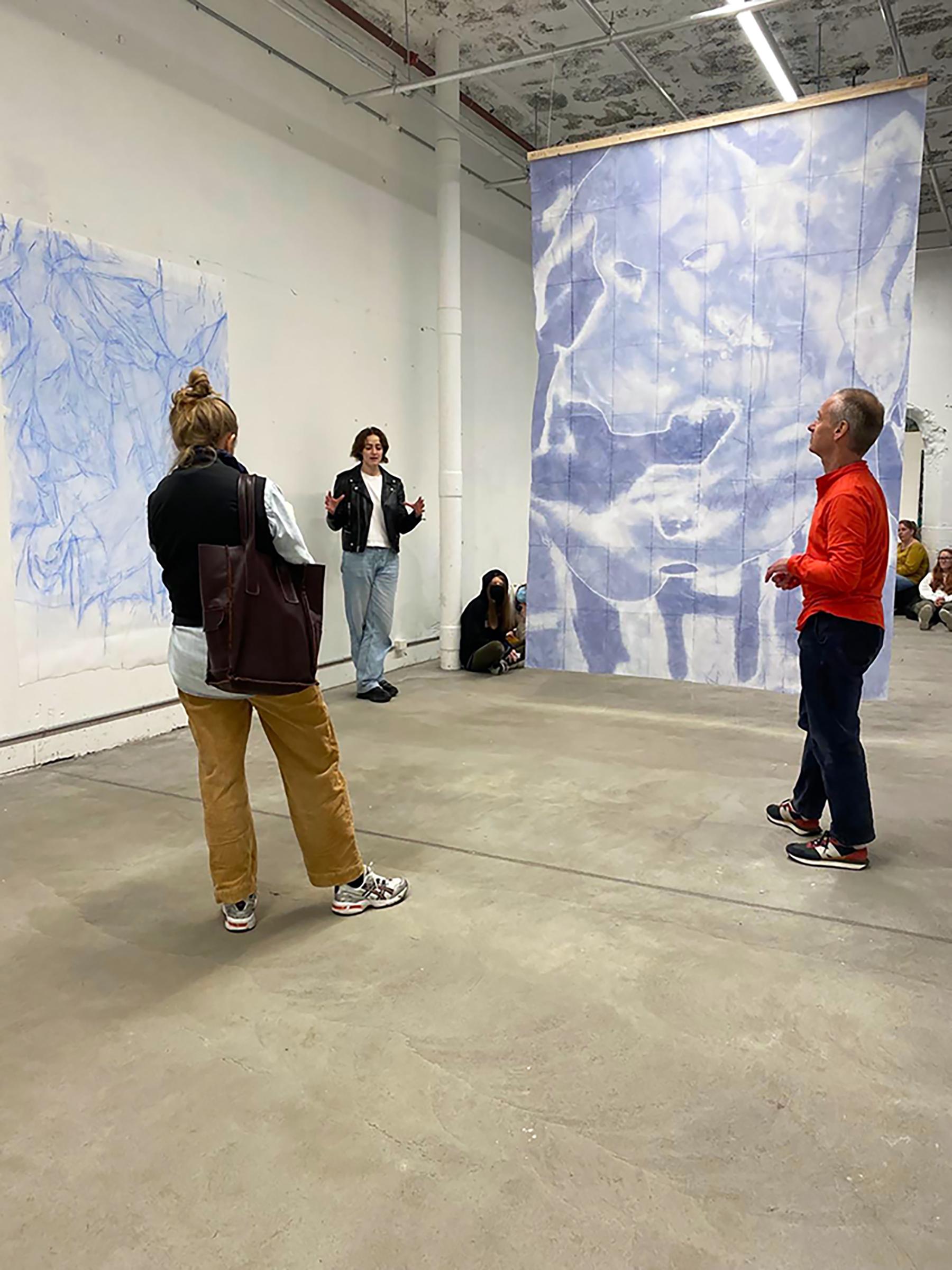 To personer står foran et stort kunstverk i en moderne utstillingshall. En av dem snakker engasjert.