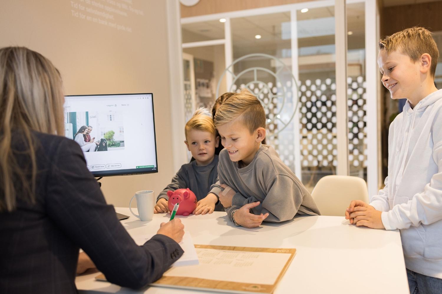 Barn som ser på en voksen som skriver på et papir ved et bord i et moderne kontor.