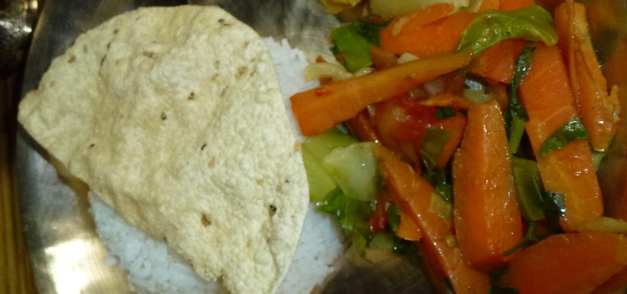 En tallerken med ris, chapati og en fargerik grønnsaksblanding med gulrøtter og kål.