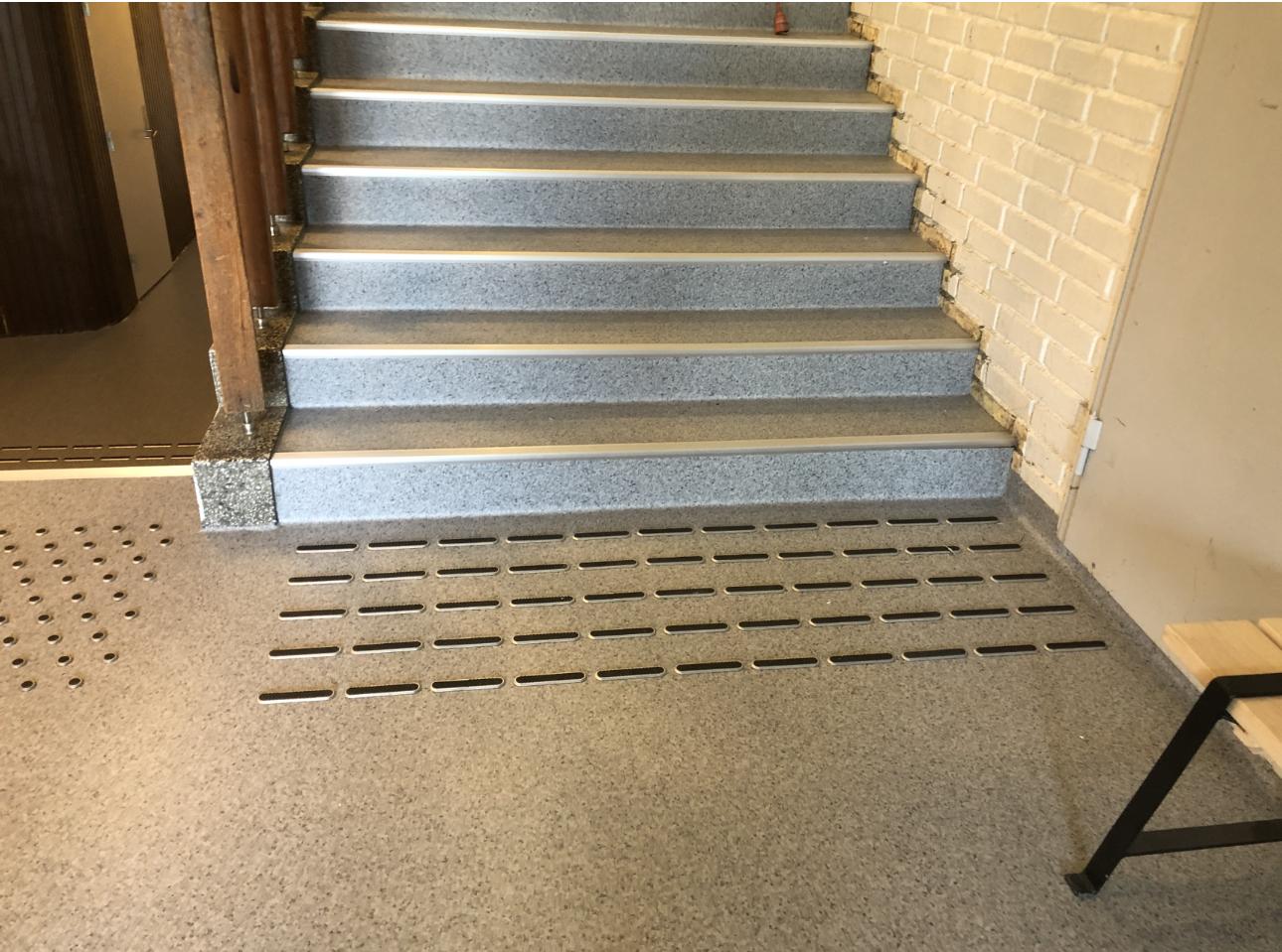 Trappen med grå trinn og gulv med perforerte plater i en bygning.