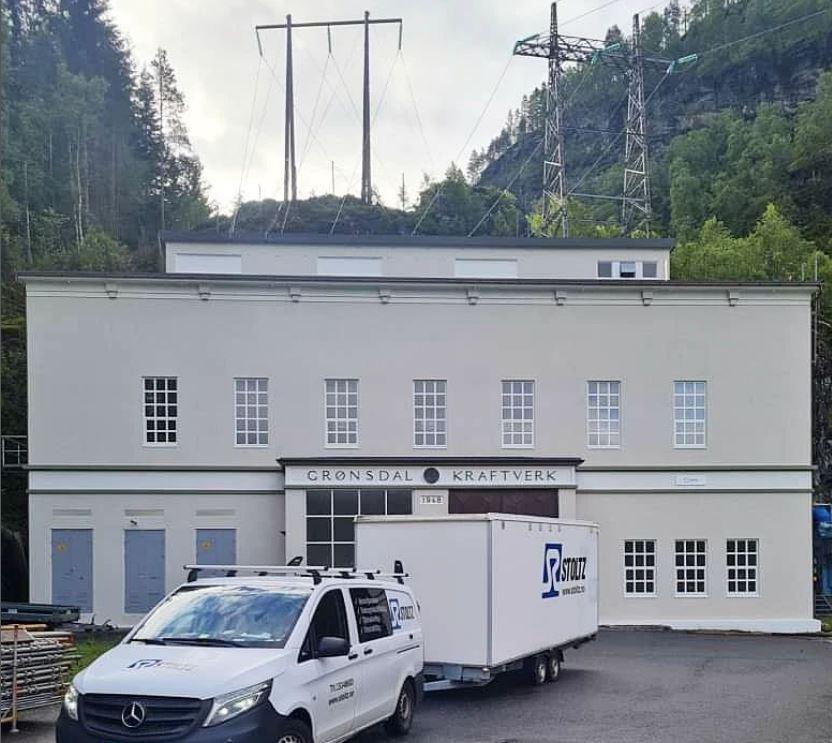 Kraftstasjon i Grøndal med en varebil parkert foran bygningen og kraftlinjer i bakgrunnen.
