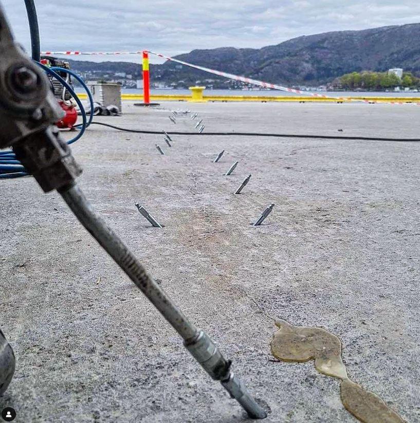 En nærbilde av en betongoverflate med metallstifter og en slange, med fjell i bakgrunnen.