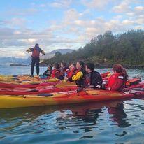 Gruppe mennesker i kajakker på vannet, med en instruktør som gir veiledning i bakgrunnen.