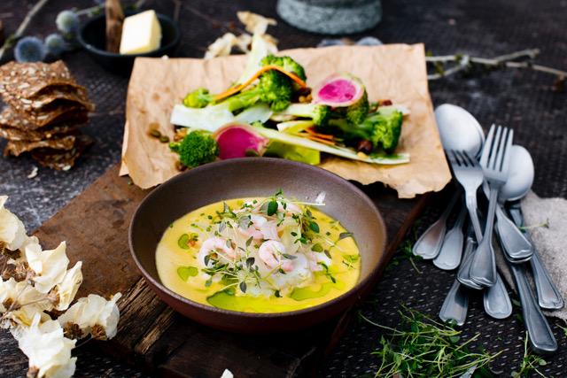 Kremet suppe med reker, urter og grønnsaker, servert med salat og knekkebrød på et rustikt bord.