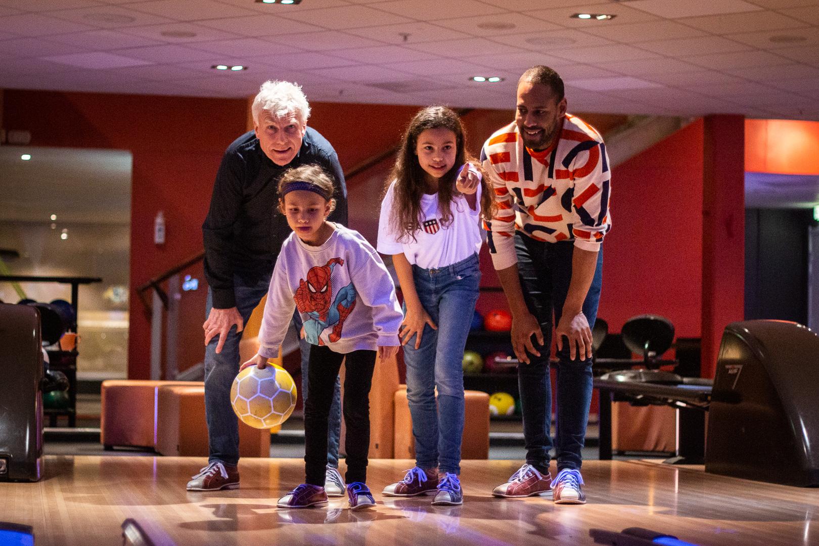 En gruppe mennesker som spiller bowling, med to barn og to voksne som står klare til å kaste en bowlingball.
