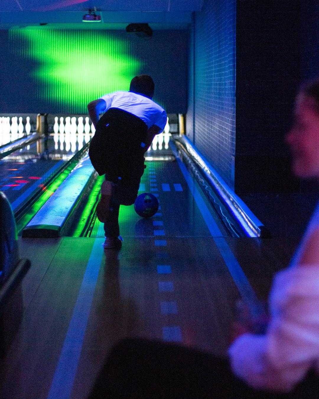 En person som bowler i en mørk bowlinghall med blått og grønt lys.
