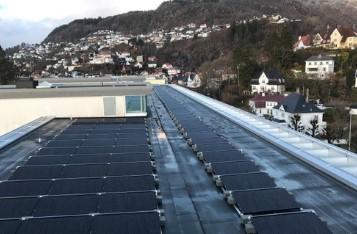 Tak med solcellepaneler og utsikt over en by med fjell i bakgrunnen.