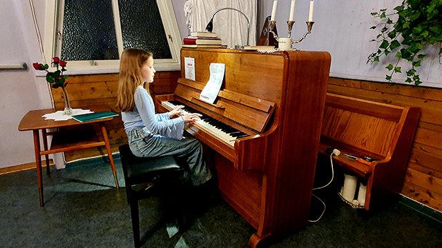 Jente som spiller piano i et rom med blomster og stearinlys på bordet.