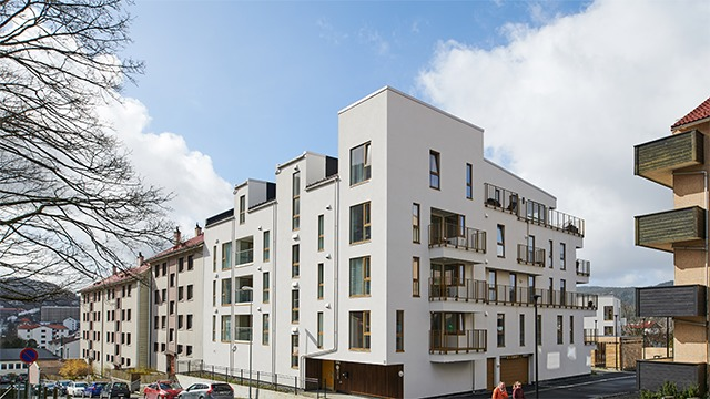 Moderne leilighetsbygg med balkonger og store vinduer under en blå himmel.