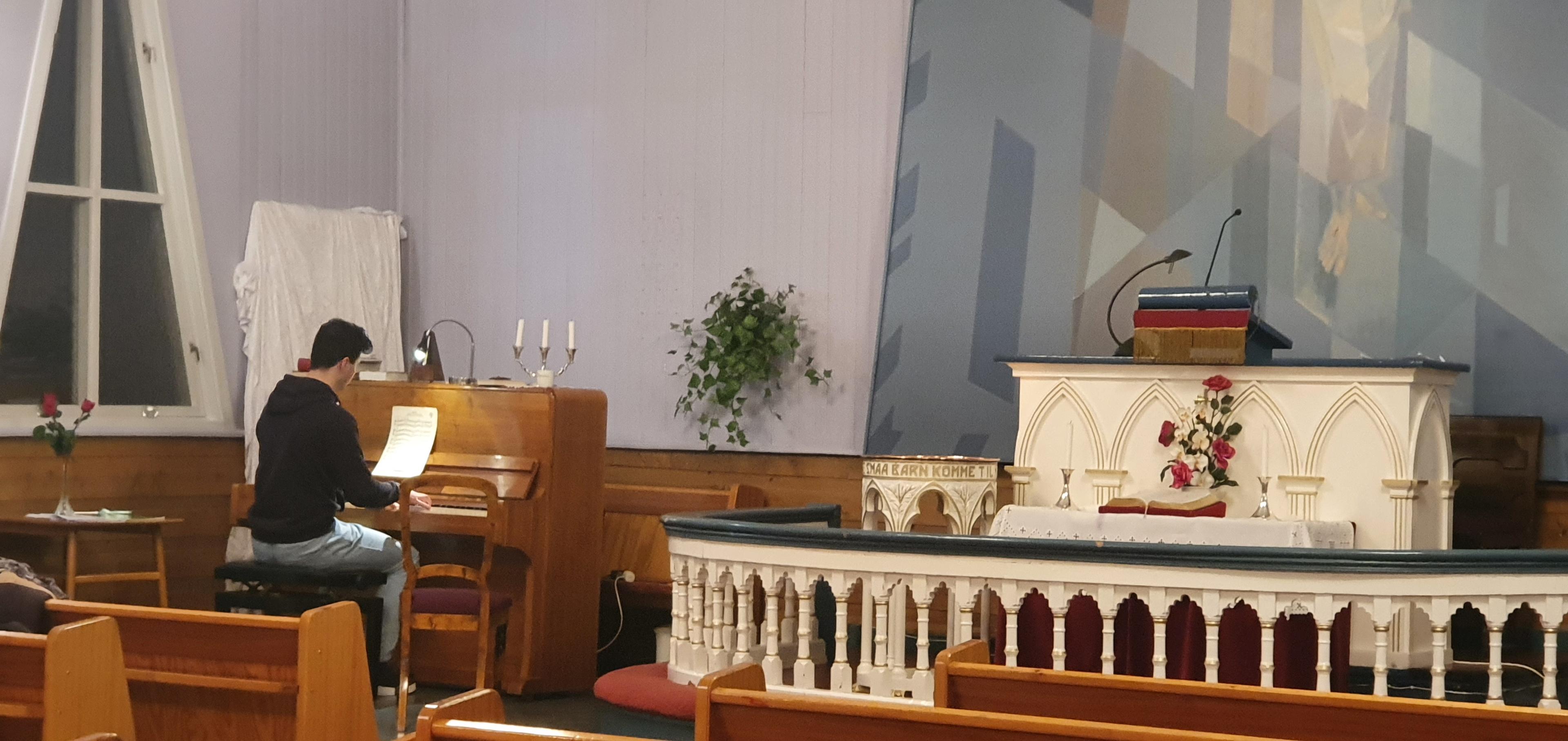 En person spiller piano i en kirke med alteret og dekorasjoner i bakgrunnen.