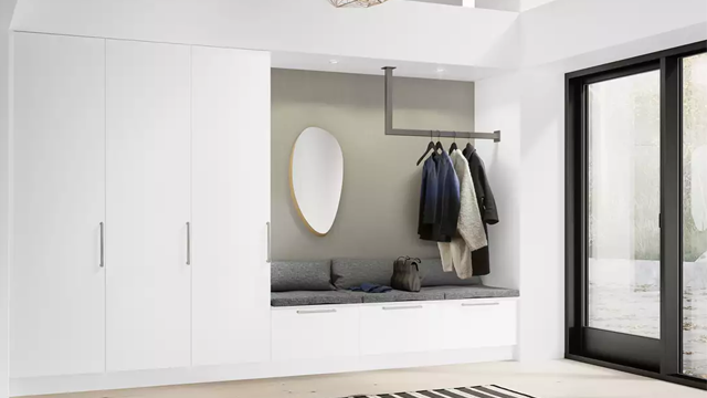 Moderne entré med hvite skap, en speil, og en benk med jakker og vesker. Store vinduer slipper inn naturlig lys.
