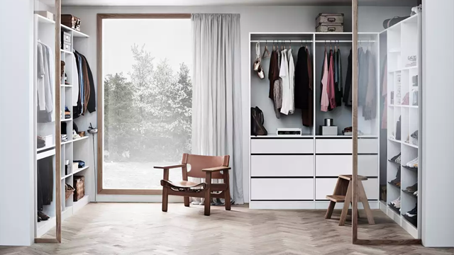 Moderne garderobe med klær, en stol og et stort vindu som gir utsikt til en hage.