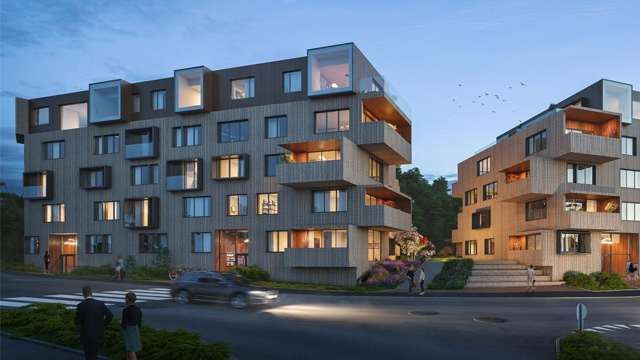 Moderne leilighetsbygg med tre etasjer, beliggende ved veien, omkranset av grøntområder og belysning om kvelden.