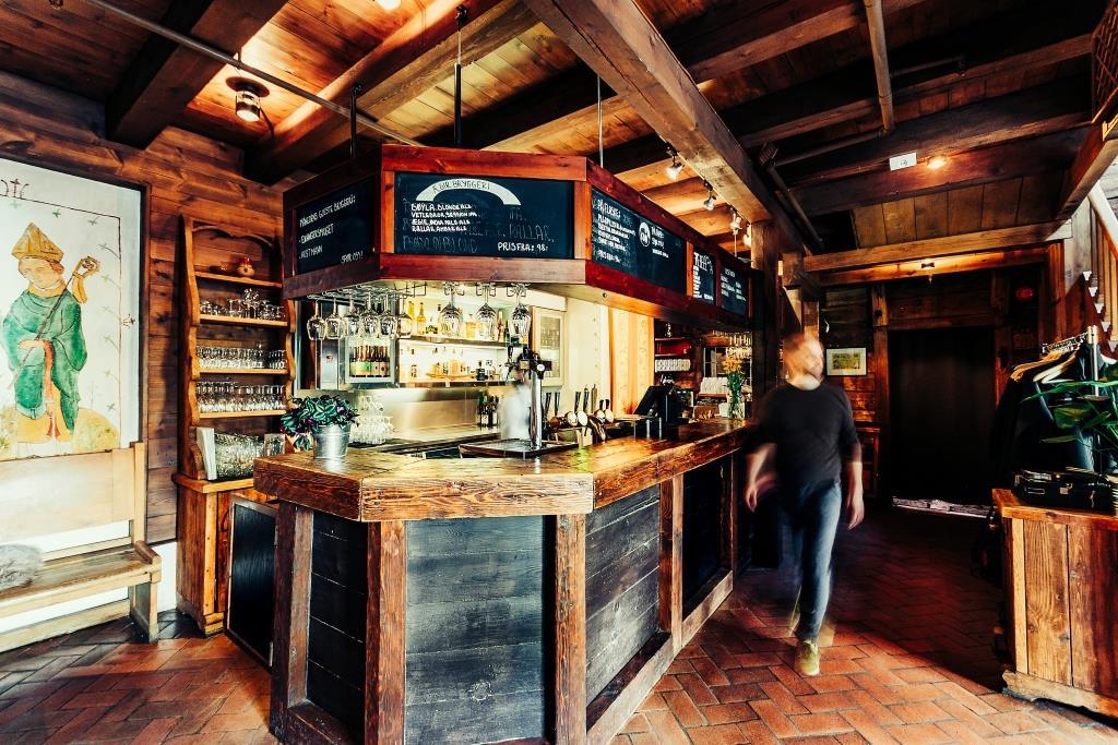 En koselig bar med treinnredning, hyller med flasker og en person som går forbi.