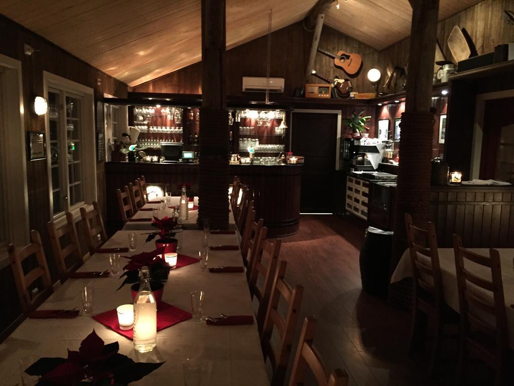 Koselig restaurantinteriør med borddekorasjoner, stearinlys og en bar med drikkevarer i bakgrunnen.