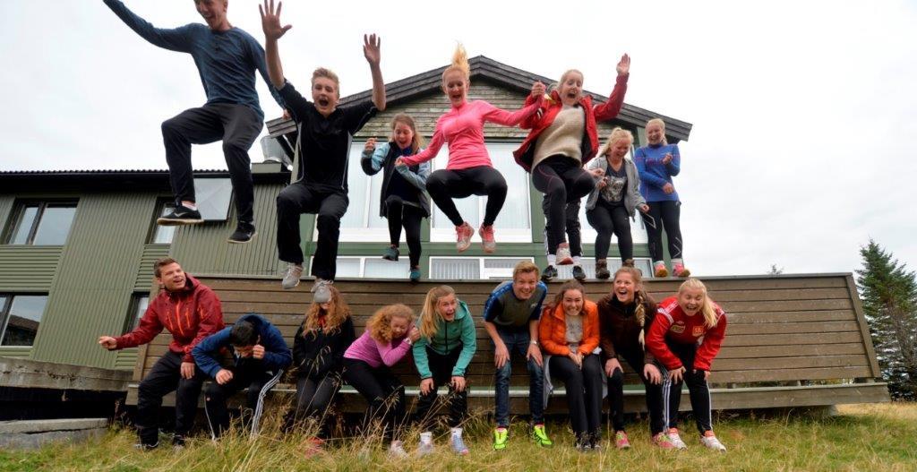 En gruppe mennesker hopper og poserer foran en bygning, med glade ansikter og fargerike klær.
