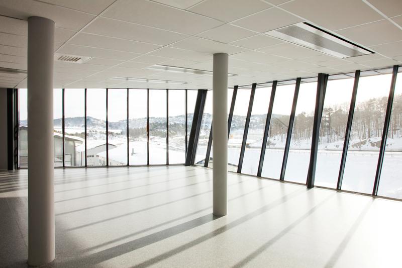 Moderne kontorlokale med store vinduer som gir utsikt over snødekte landskap og fjell.