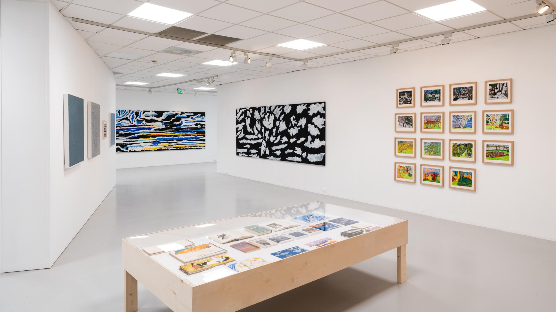 Moderne kunstgalleri med malerier på veggene og en utstillingsbord med kunstverk i midten.