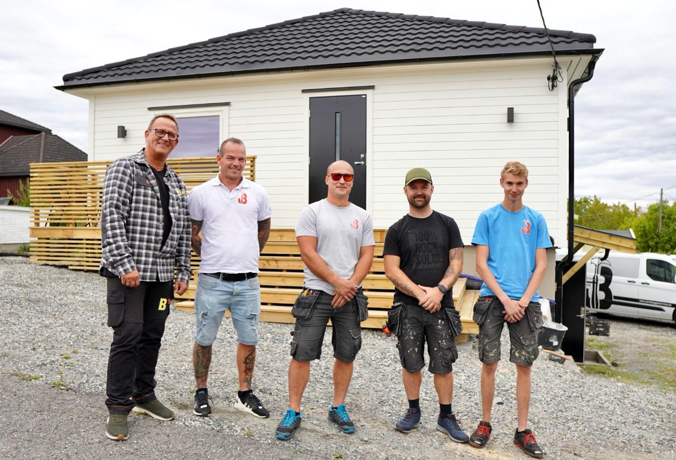 Fem menn står foran et nyoppusset hus med tredekk og grusvei. De smiler og ser mot kameraet.