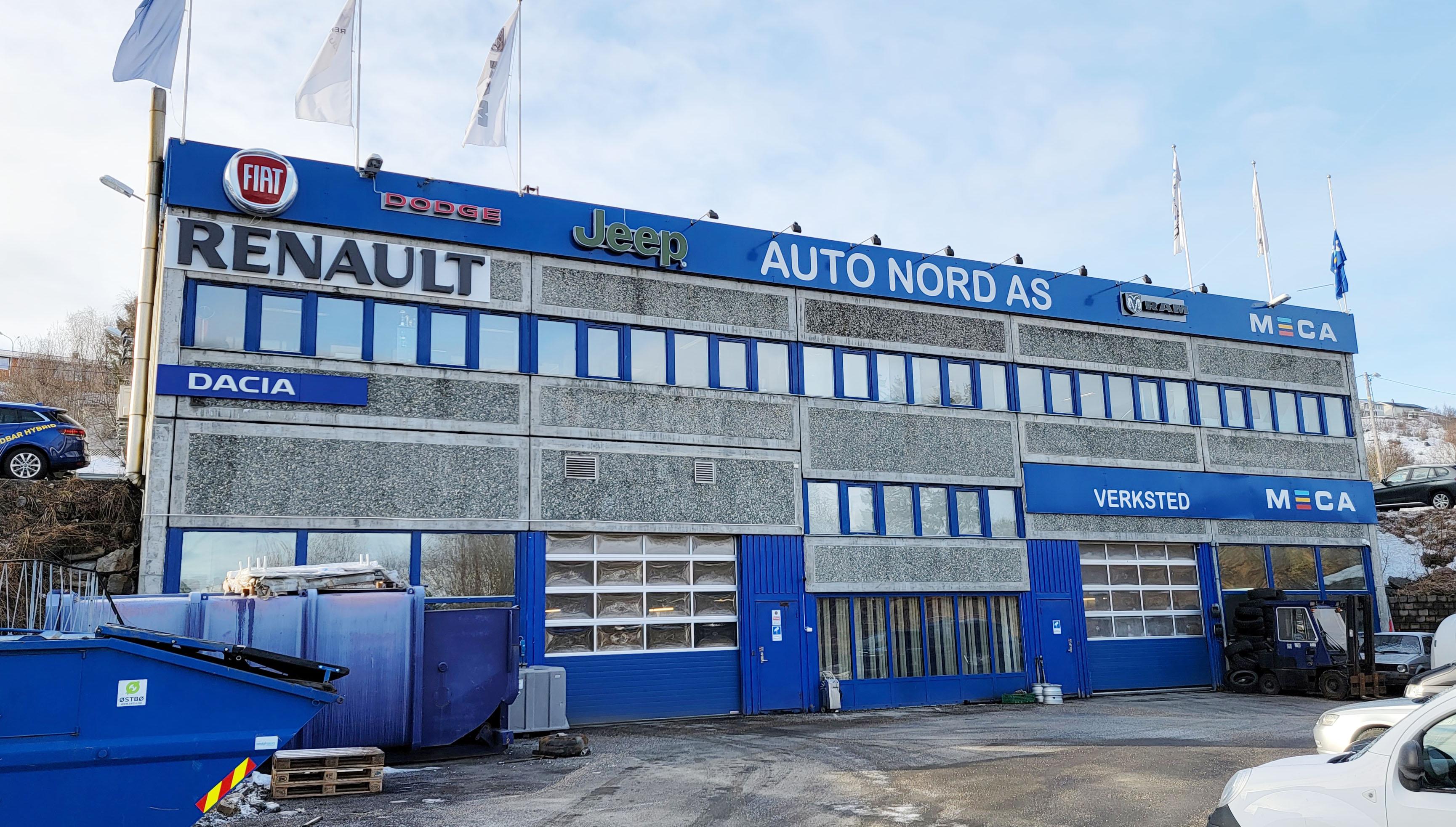 Bygning med Auto Nord AS-skilt, som viser Renault, Dacia og Ford, med snø på bakken og blå himmel.