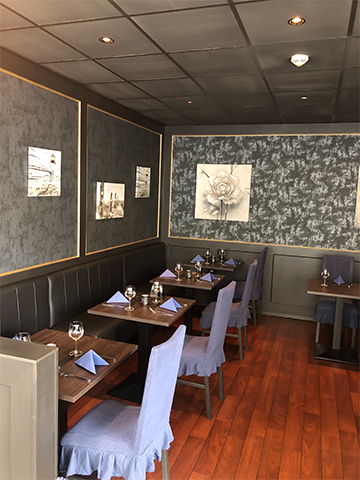 En koselig restaurant med mørke vegger, bord dekket med blå servietter og stoler med blå trekk.