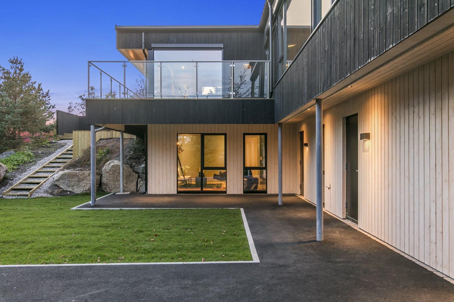 Moderne hus med terrasse, hage og steintrapp, beliggende i naturskjønne omgivelser ved skumring.