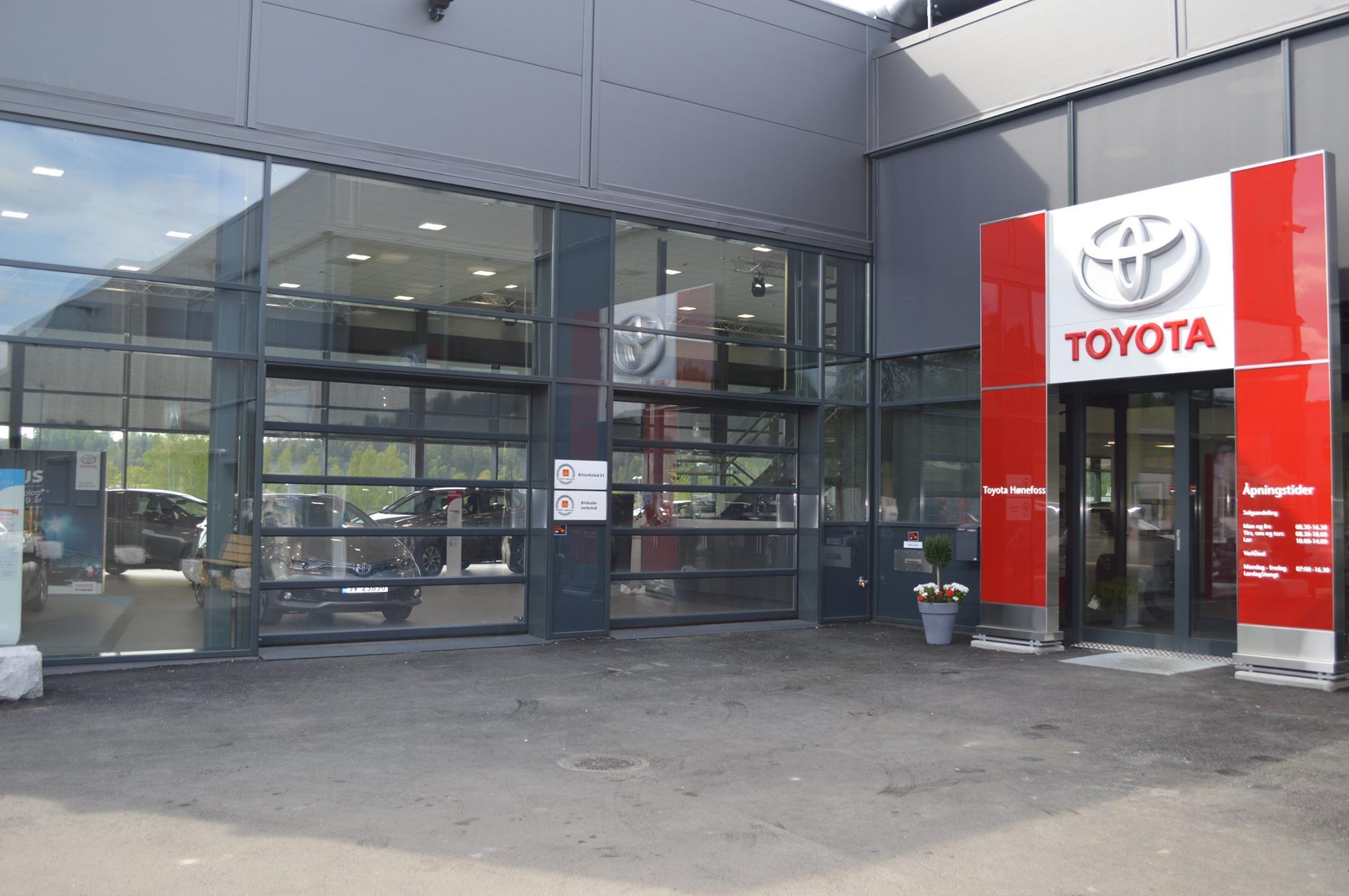 Inngangspartiet til en Toyota-forhandler med store vinduer og logo. Parkerte biler er synlige i bakgrunnen.