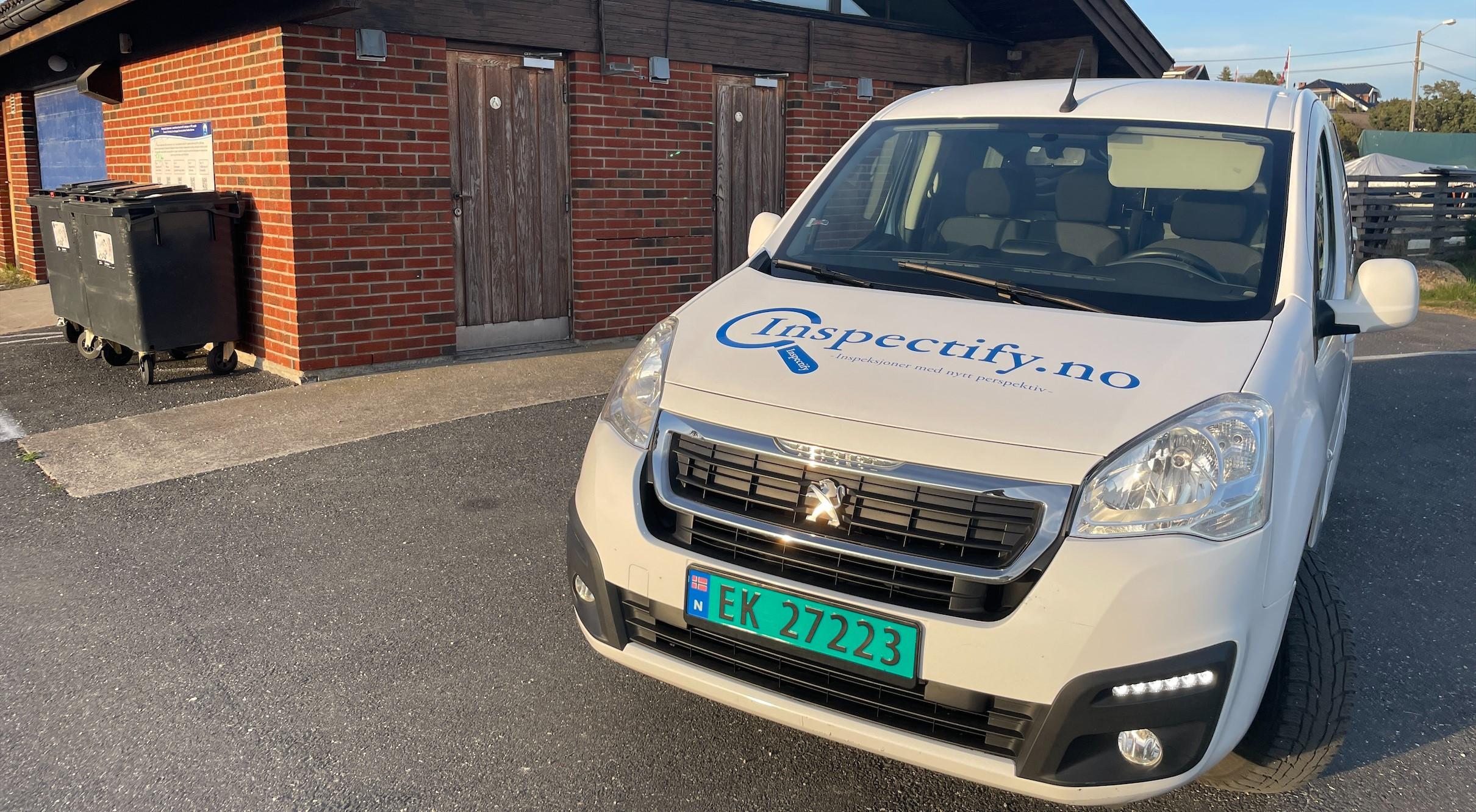 En hvit varebil med logoen "Electricity40" parkert foran en bygning med søppeldunker.