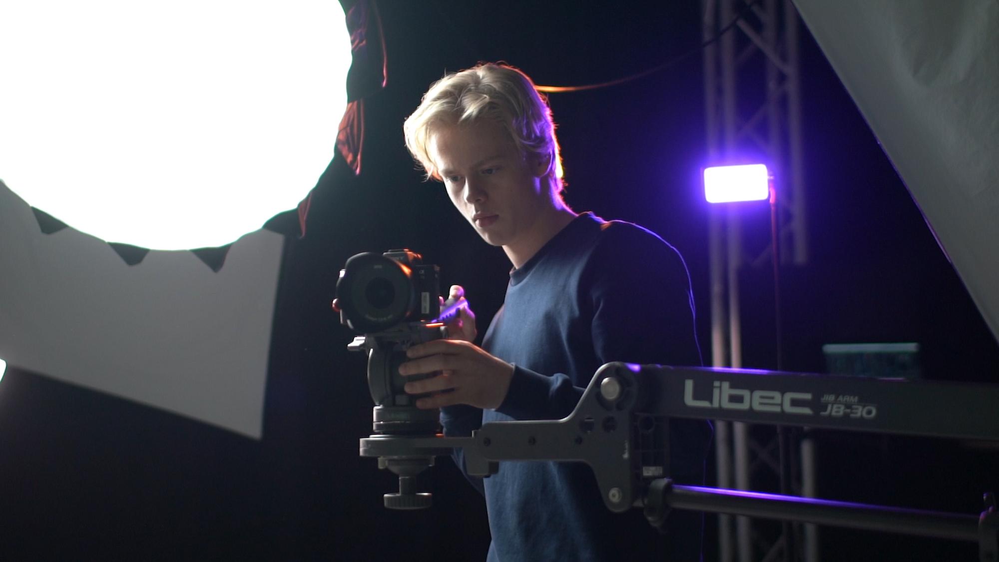 En fotograf justerer kameraet sitt under en fotoshoot med lysutstyr i bakgrunnen.