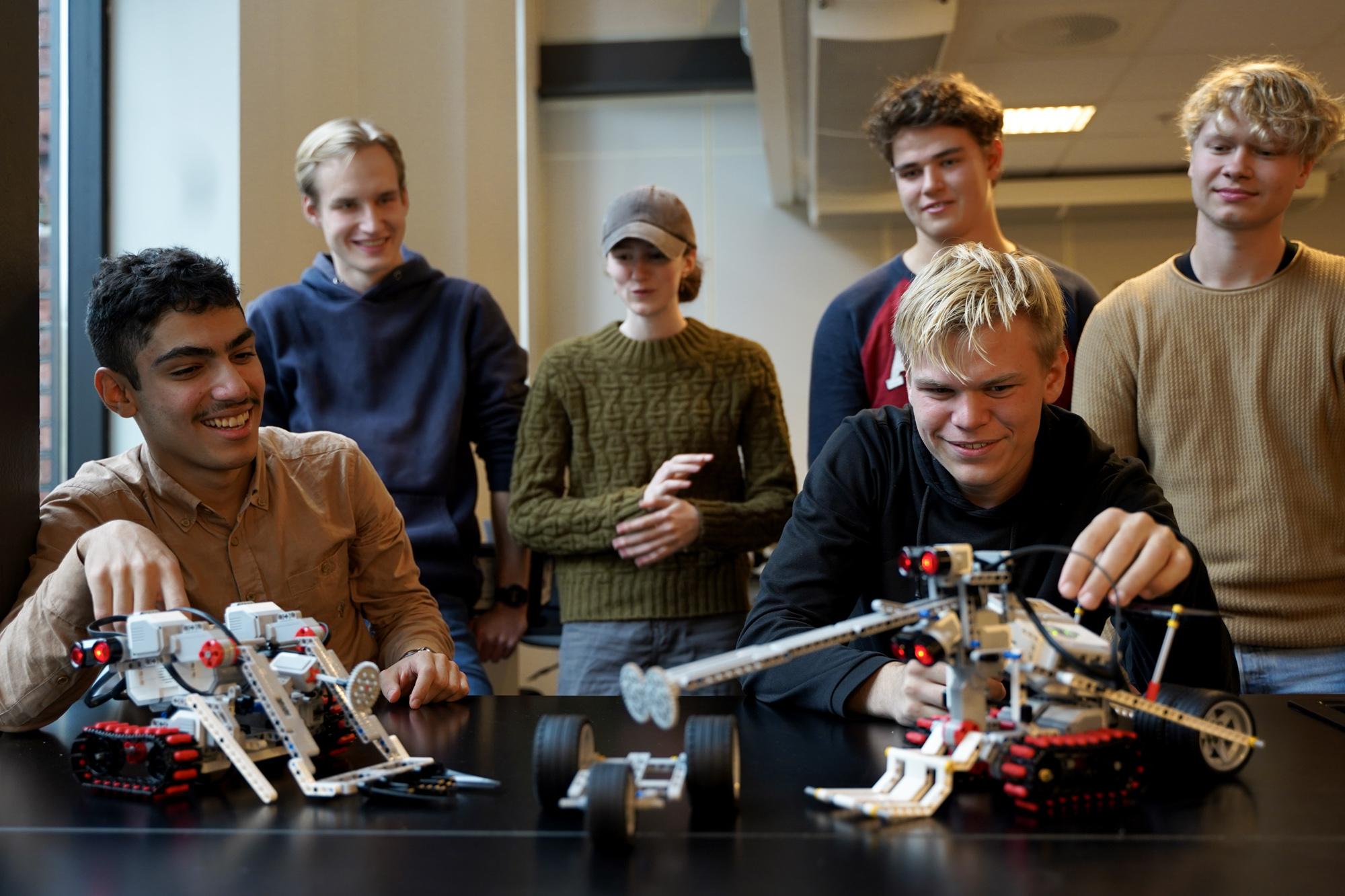 Ungdommer jobber med roboter i et klasserom, med fokus på to modeller og entusiasme i ansiktene deres.