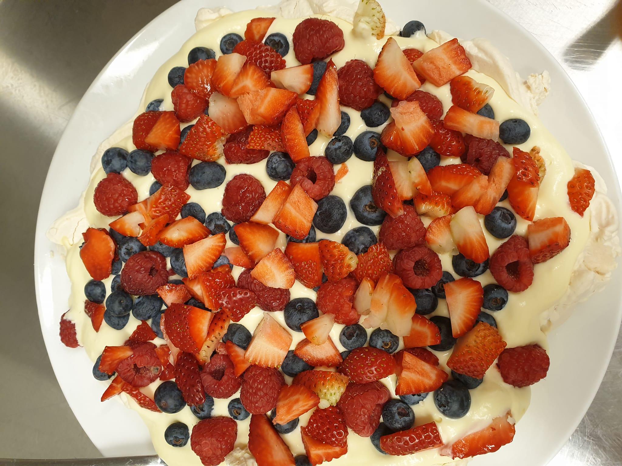 En pavlova med friske jordbær, bringebær og blåbær på en kremet bunn.