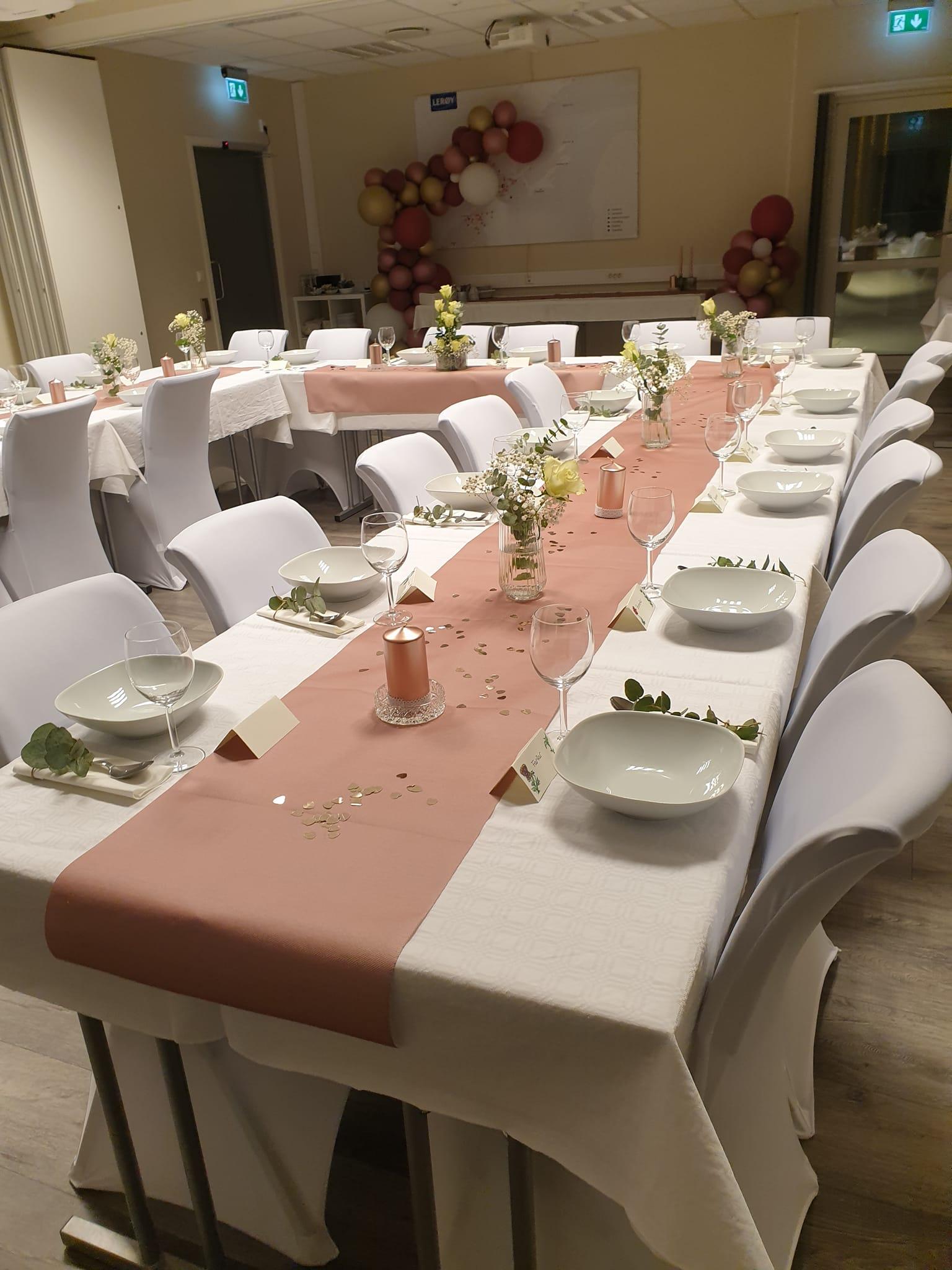 Borddekorasjon med hvite stoler, duker og blomsterarrangementer i et festlokale.