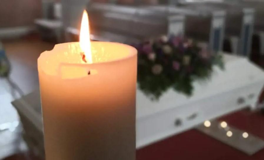 Lysende stearinlys foran en hvit kiste med blomsterdekorasjon i bakgrunnen.
