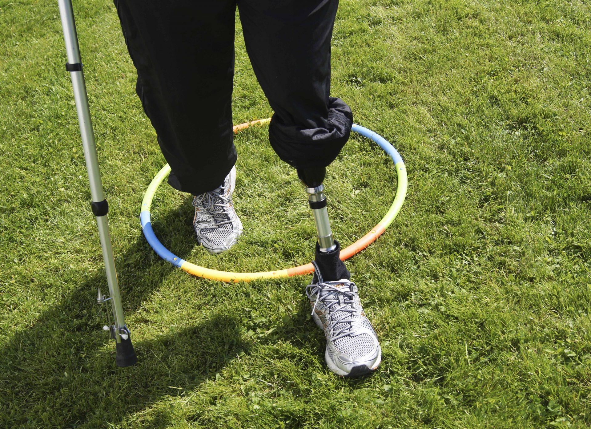 En person med protesefot står på gresset med en rullestav og en hula-hoop rundt benet.