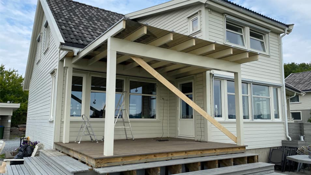 Moderne hus med terrasse og takoverbygg, bygget i lys farge, med stiger og treverk synlig.