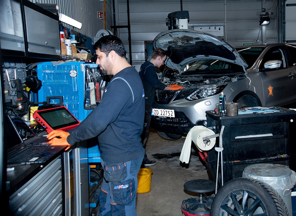 To personer jobber i et bilverksted, en bruker en laptop mens den andre jobber med en bilmotor.