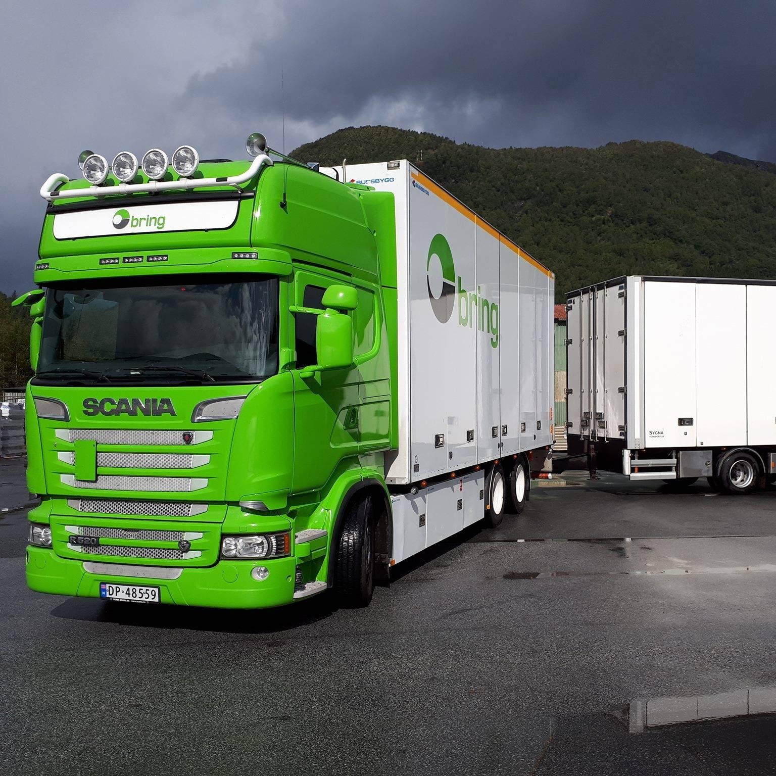 Grønn Scania lastebil med tilhenger parkert ved en lasteplass under en mørk sky.