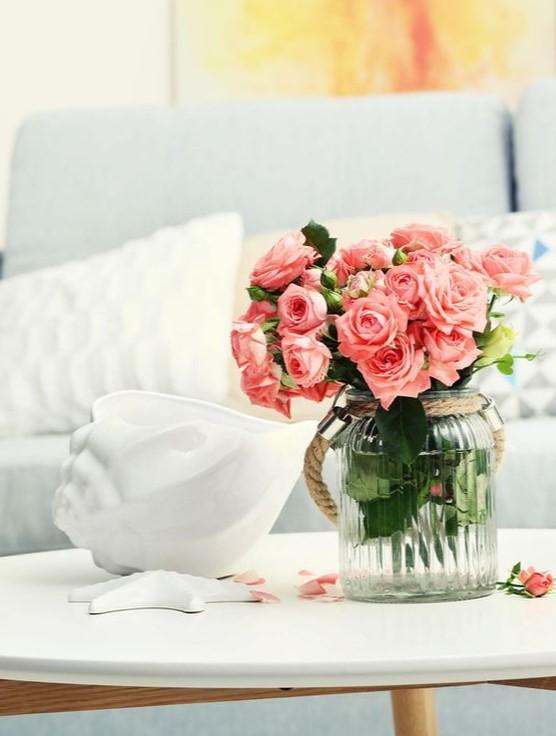 En vase med rosa roser står på et bord, ved siden av en hvit skulptur og en myk sofa i bakgrunnen.