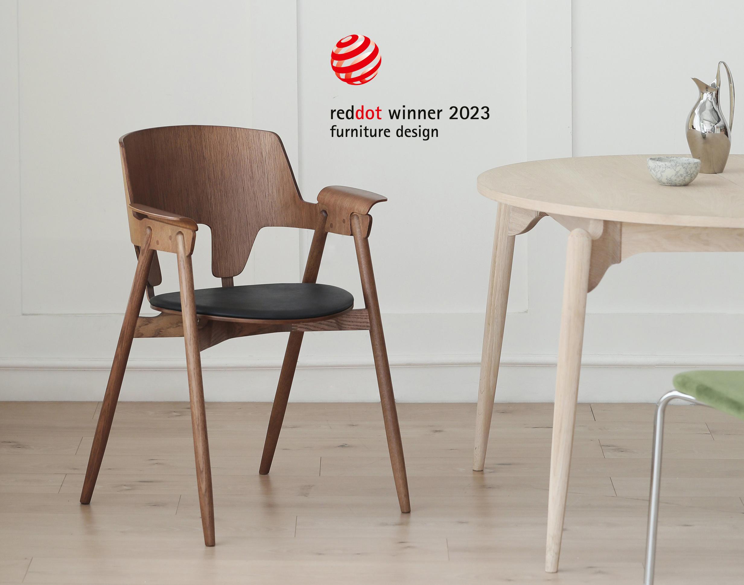Moderne stol i tre med svart sete, plassert ved et lyst bord i et stilrent rom. Red Dot-vinner 2023.