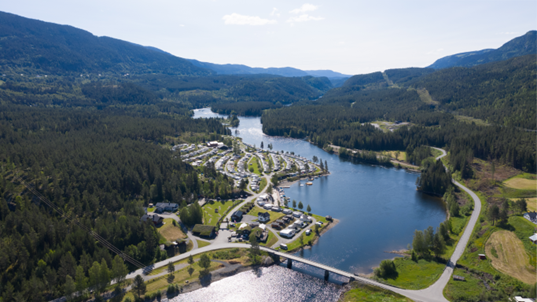Luftbilde av en campingplass ved en innsjø, omringet av fjell og skog i et naturskjønt landskap.