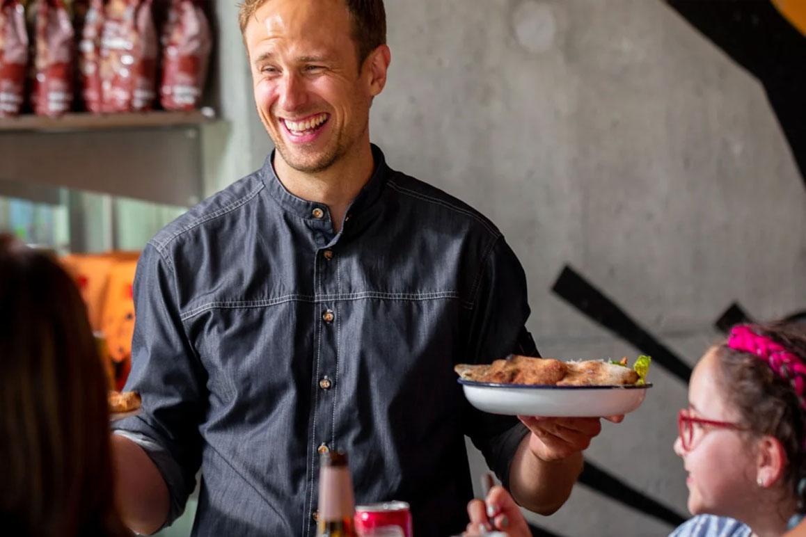 En smilende servitør som serverer mat til gjester i en restaurant.