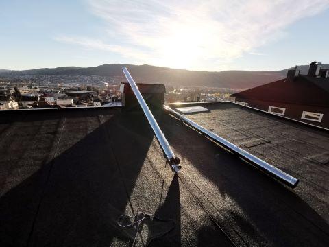 Tak med solpaneler og utsikt over byen i solnedgang. Fjell i bakgrunnen.